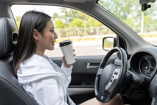 Young woman drinking coffee while driving her car