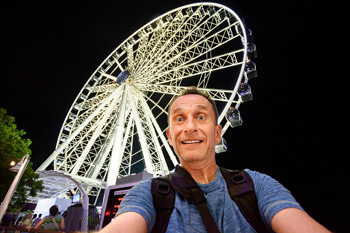 Mid adult man taking a selfie in front of a ferris wheel at night (Miami downtown, Florida)