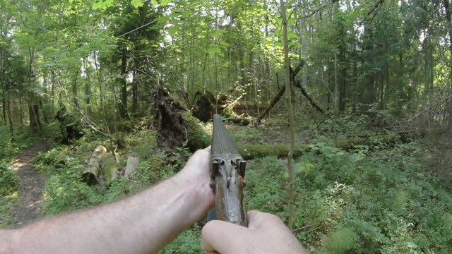 A man pointing a shot gun on the woods