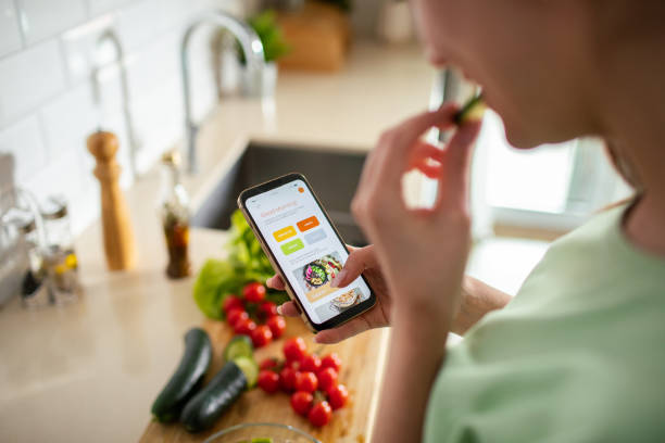 istock Young woman using a diet app on her phone while preparing a healthy food dish at home 1490092003
