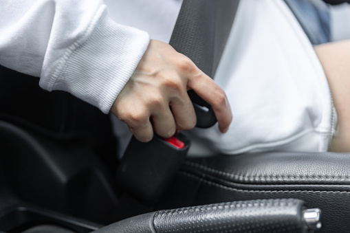 Woman fastens car seat belt with hand. Compliance with safety rules for driving. Protection of female person in vehicles. Fasten your body with a seat belt in the car. Road safety regulations concept