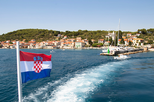 Prvic Luka, Croatia - July 22, 2022: Croatian flag on a ferry leaving the small town Luka on Prvic island