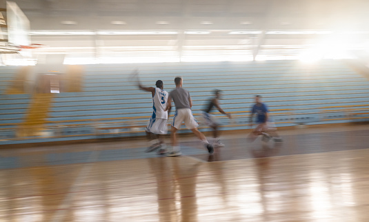 A group of professional basketball players training on an indoor court. They are in two groups and playing basketball game. Blurred motion photo. Concept of team sport and healthy lifestyle.