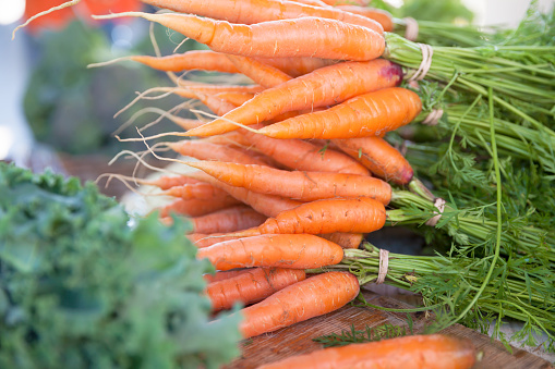 Bunches of fresh orange carrots, with kale to the side, on display at a farmer's market