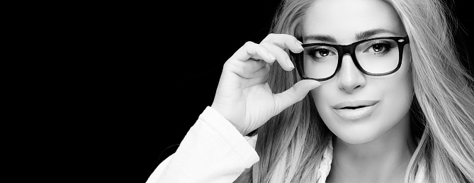 Gorgeous middle-aged woman in eyeglasses. Vision correction and eye care concept. Close up monochrome portrait isolated on black with copy space