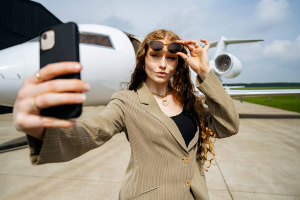 businesswoman posing for selfie in front of corporate jet - corporate jet imagens e fotografias de stock