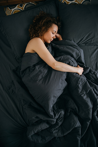 A young woman sleeps in the fetal position in the morning on an ergonomic bed. Comfortable sleep with health benefits of a cute girl in a cozy atmosphere, top view. lazy weekend