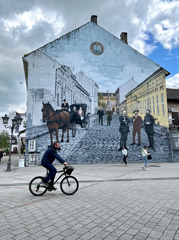 Novi Sad, Serbia - April 25, 2023: Man cycling on the street in front of beautiful mural