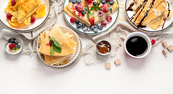 Variety of fresh crepes with chocolate, jam, fruits and berries on white background. Homemade delicious crepes. Top view. Panorama with copy space.