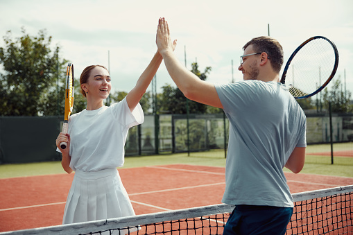 Handsome man and beautiful woman are giving high five and smiling. Sports active game with friends. Tennis player in action. Tennis match. Active leisure game. Weekend activity for recreation