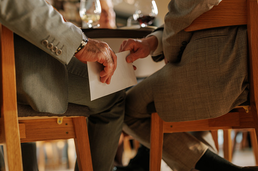 A close up shot of the hands of a businessman handing money to another businessman in an envelope under the table in a cafe.
