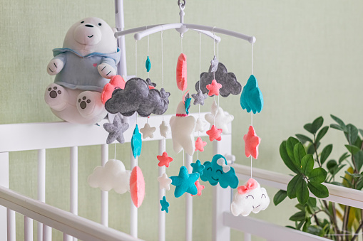 Baby crib mobile with stars, clouds and moon. Kids handmade toys above the newborn crib. First baby eco-friendly toys made from felt hanging in light room.