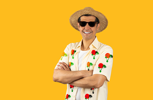 Latin man on vacation wearing floral shirt hat sunglasses over isolated yellow background happy face smiling with crossed arms looking at the camera. Positive person.