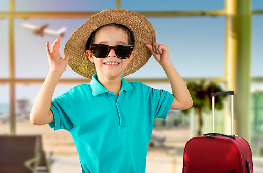 Child on vacation wearing blue t-shirt hat sunglasses at airport happy face smiling and looking at the camera. Positive person