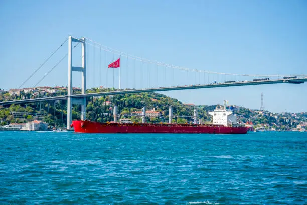 Photo of A cargo ship sails under a bridge in Istanbul on a summer and sunny day.