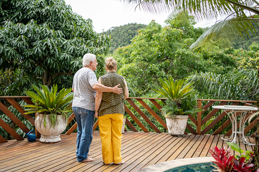 Rear view of a senior couple standing by the poolside deck of their vacation rental and looking at the scenic view
