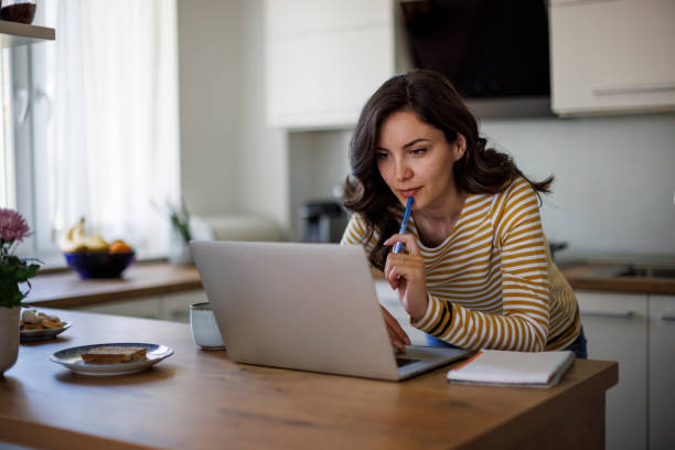 Giovane donna che usa un laptop mentre lavora da casa - foto stock