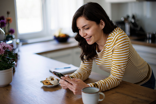 Young smiling woman with mobile phone in kitchen