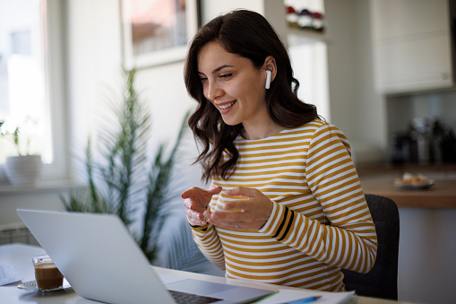 Young smiling woman with bluetooth headphones having video call at home