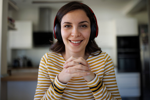 Smiling confident young woman with bluetooth headphones having having video call at home