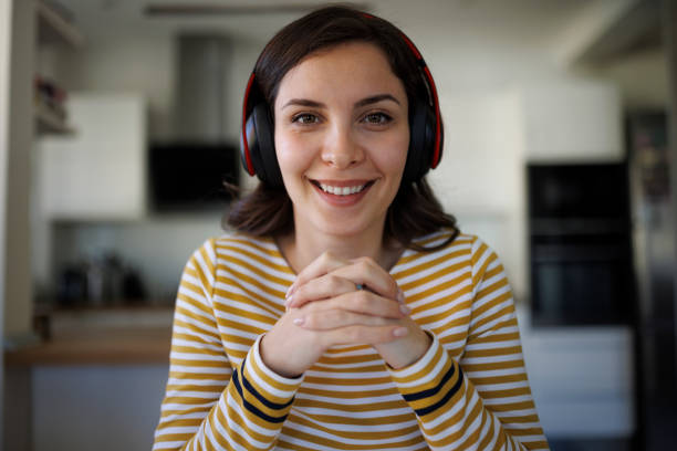 Smiling confident young woman with bluetooth headphones having having video call at home stock photo