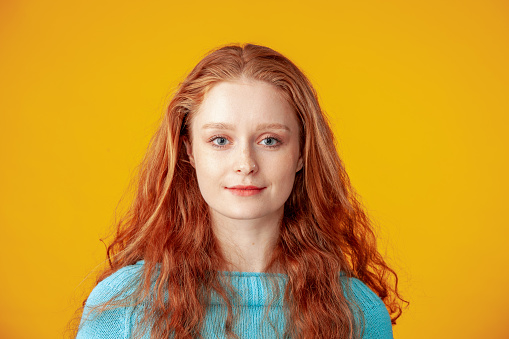 Close-up studio portrait of a young attractive cheerful red-haired woman against a yellow background