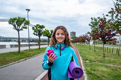 teenage girl walking happily on the running track after training, carrying a bottle and a training mat