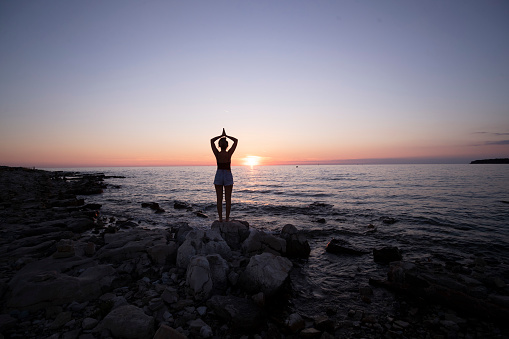 Silhouette of young woman practicing yoga and meditating on the beach