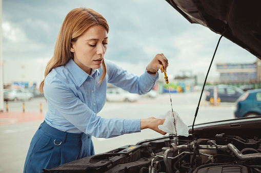 Woman driver checking level of oil on a car engine dipstick