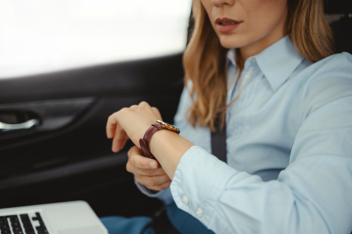 Business-style woman looks at her watch while sitting in the backseat of a car during her morning commute