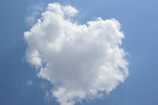 a small cloud in the shape of a heart against the blue sky. The rays of the sun are visible from under the clouds. heart is a symbol of love, fidelity, sympathy and strong friendships