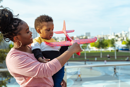 African American mother playing with her cute little son and holding an airplane toy