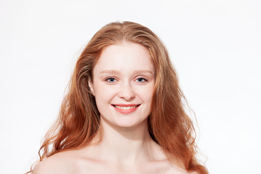 Close-up studio portrait of a young attractive cheerful red-haired woman against a white background