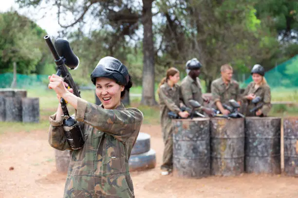 Photo of Happy woman wearing uniform and holding gun ready for playing with friends on paintball