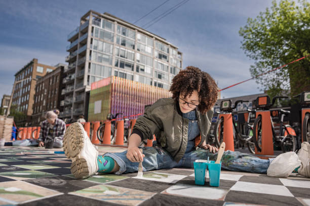 Two Female artists painting large wall mural. They are dressed in casual work clothes. Exterior of public  sidewalk in downtown of large North American City.