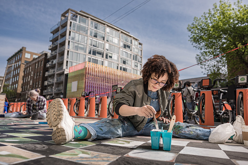 Two Female artists painting large wall mural. They are dressed in casual work clothes. Exterior of public  sidewalk in downtown of large North American City.