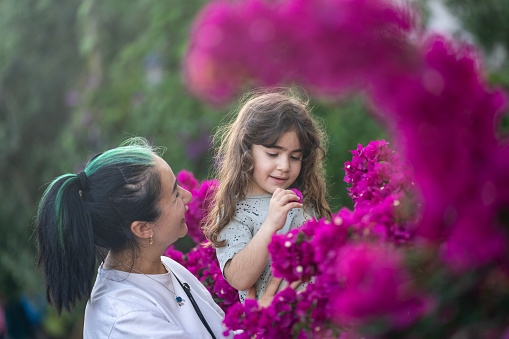 Photo of mother and 4,5 years old daughter playing with bougainvillea flowers in outdoor. Shot under daylight. Selective focus on models.