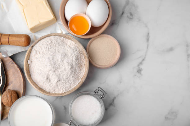 istock Bowl of flour and other ingredients in white marble table, flat lay. Space for text 1490188410
