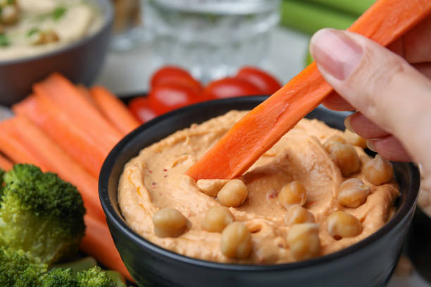 istock Woman dipping carrot stick into hummus at table, closeup 1490188760