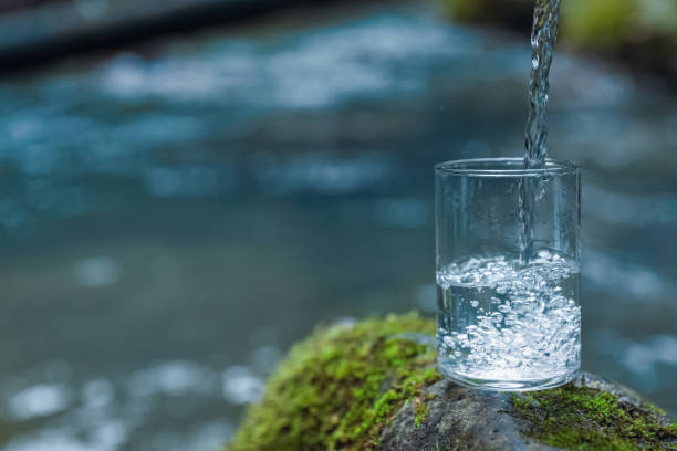 istock Fresh water pouring into glass on stone near river. Space for text 1490197508
