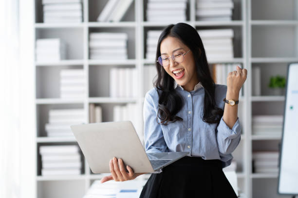 istock Overjoyed Asian businesswoman in glasses celebrating success withe her laptop computer. 1490207574