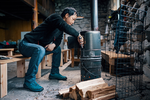 Mid-adult man preparing a fire in a rustic cabin in the wilderness of Japan