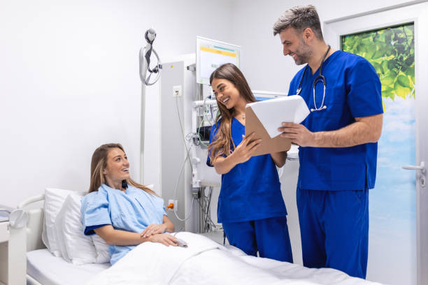 istock Doctors in uniform with stethoscope using clipboard standing in hospital ward with patient resting in bed on background. Practitioner checking patient data 1490237820