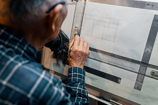 Senior male architect working at a drafting table drawing blueprints by hand