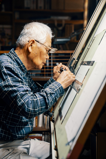 Senior male architect working at a drafting table drawing blueprints by hand