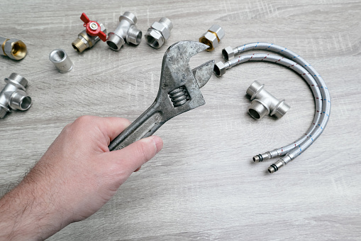 Plumbing services, plumber at work. Close-up of plumber hands with wrench over plumbing tools background. Concept of repair and technical assistance.
