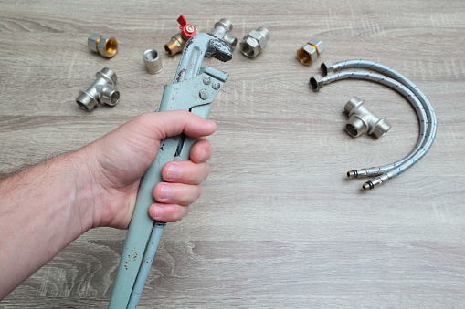 Plumbing services, plumber at work. Close-up of plumber hands with wrench over plumbing tools background. Concept of repair and technical assistance.