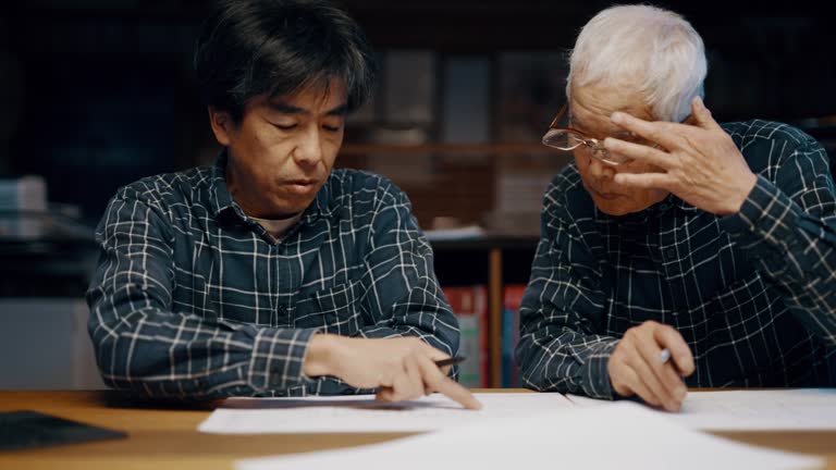 Senior father and mature son looking at blueprints