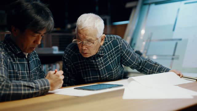 Mature man and senior father looking at blueprints on a digital tablet