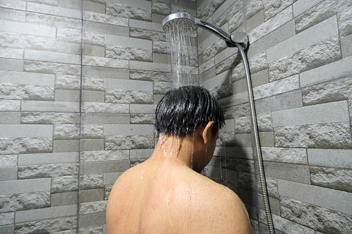 Indonesian man taking shower viewed from back